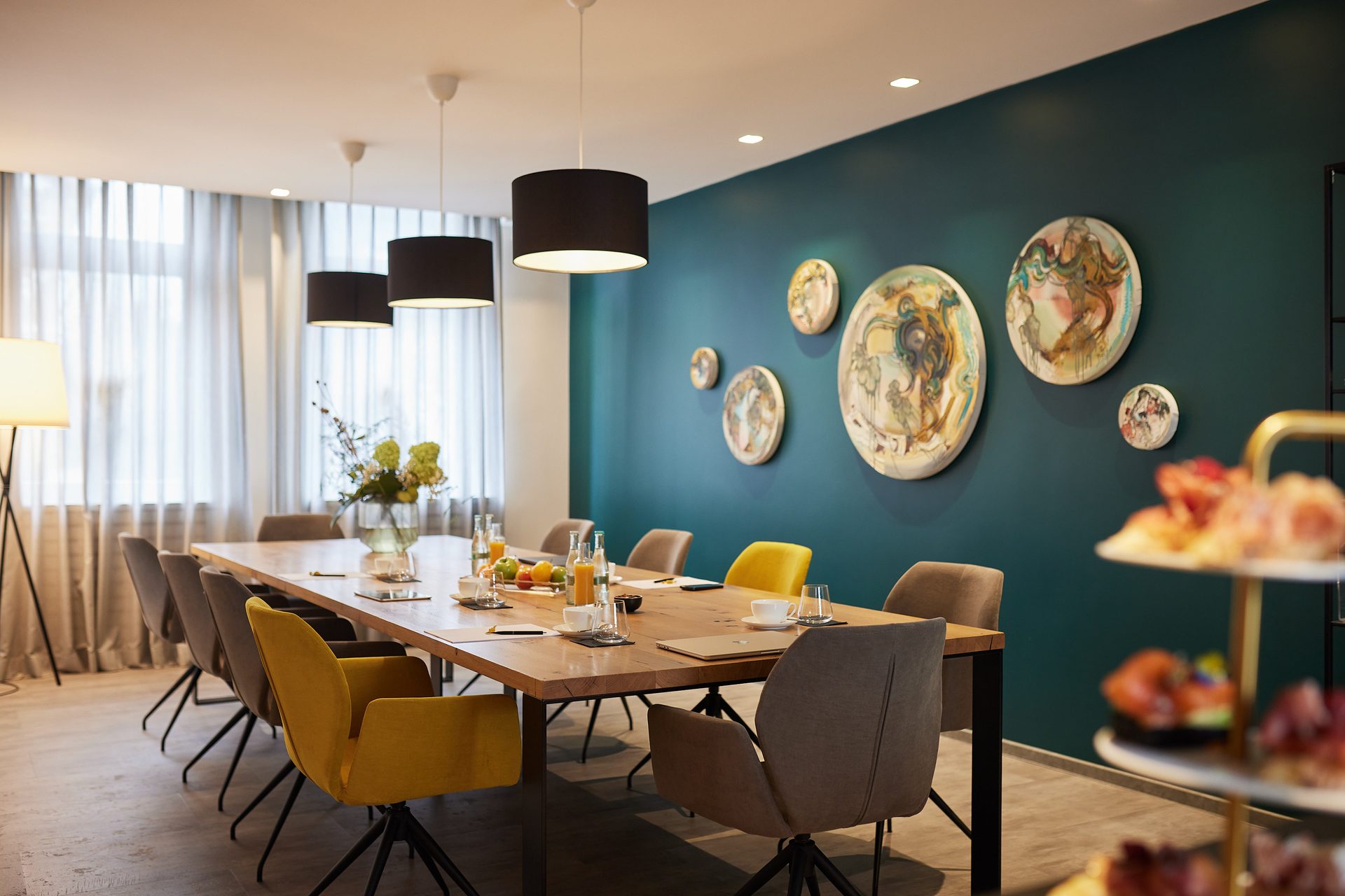 Meetingraum in Schwetzingen — die lange Tafel im Studio mit Notizblöcken, Karaffen und Tassen vor der türkisen Tellerwand